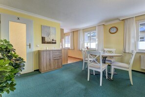 Una habitación con una mesa de comedor y sillas, un mueble bajo, una planta y un reloj en la pared.