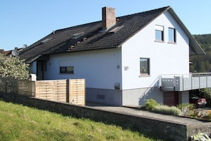 A two-story white house with a sloped roof, a wooden fence, and a small garden area. - Holiday apartment in Rhön with 2 bedrooms (Oberelsbach)