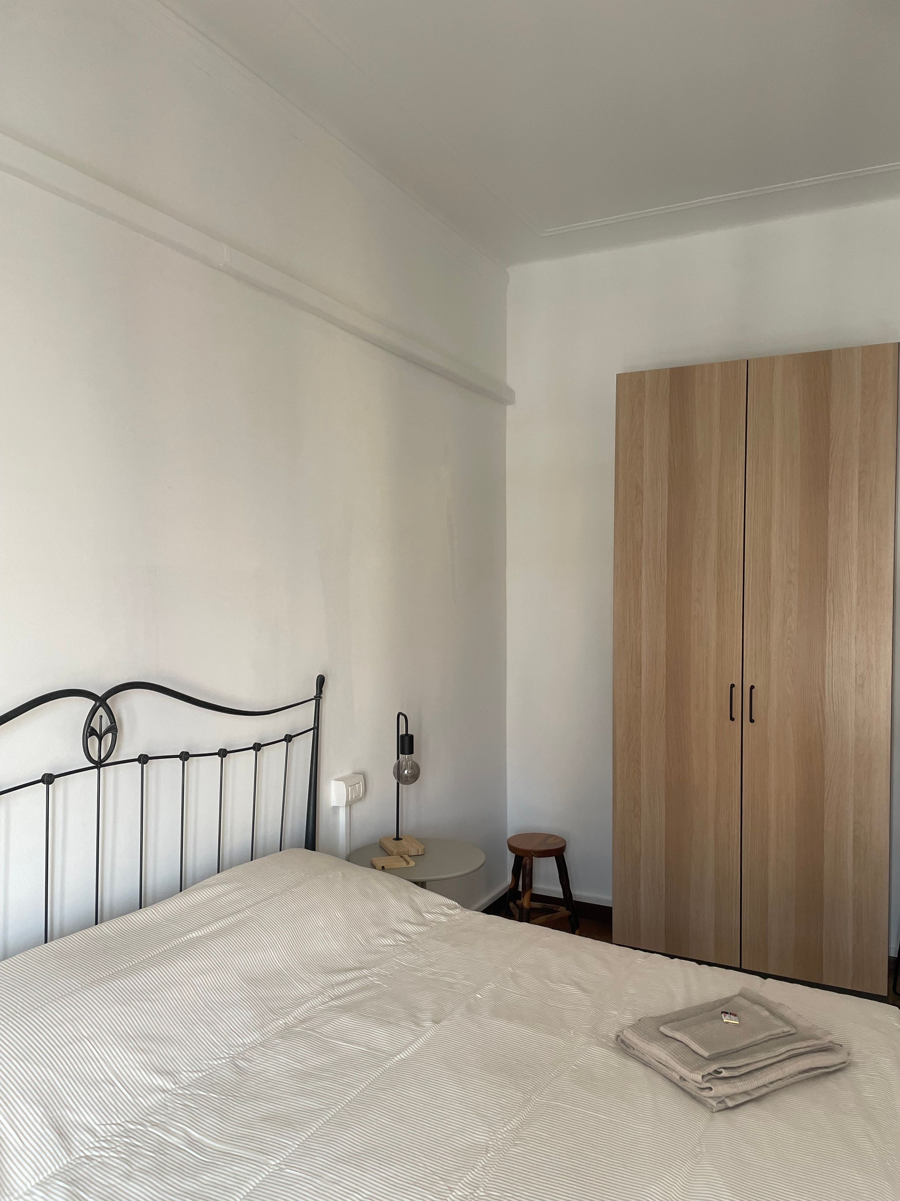 Una camera da letto con un letto, un armadio in legno, un comodino con una lampada e uno sgabello.