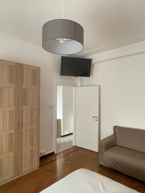 Una stanza con un armadio in legno, un divano, una televisione a muro e una porta che dà su un'altra stanza.