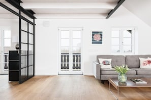 A modern living room with a grey sofa, a coffee table, and a black bookshelf. There is a white door leading to a balcony with a railing. - Zum Wehnerbauer - Ammersee (Utting, OT Holzhausen)