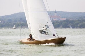 Un velero en aguas tranquilas con un edificio distante en la orilla.