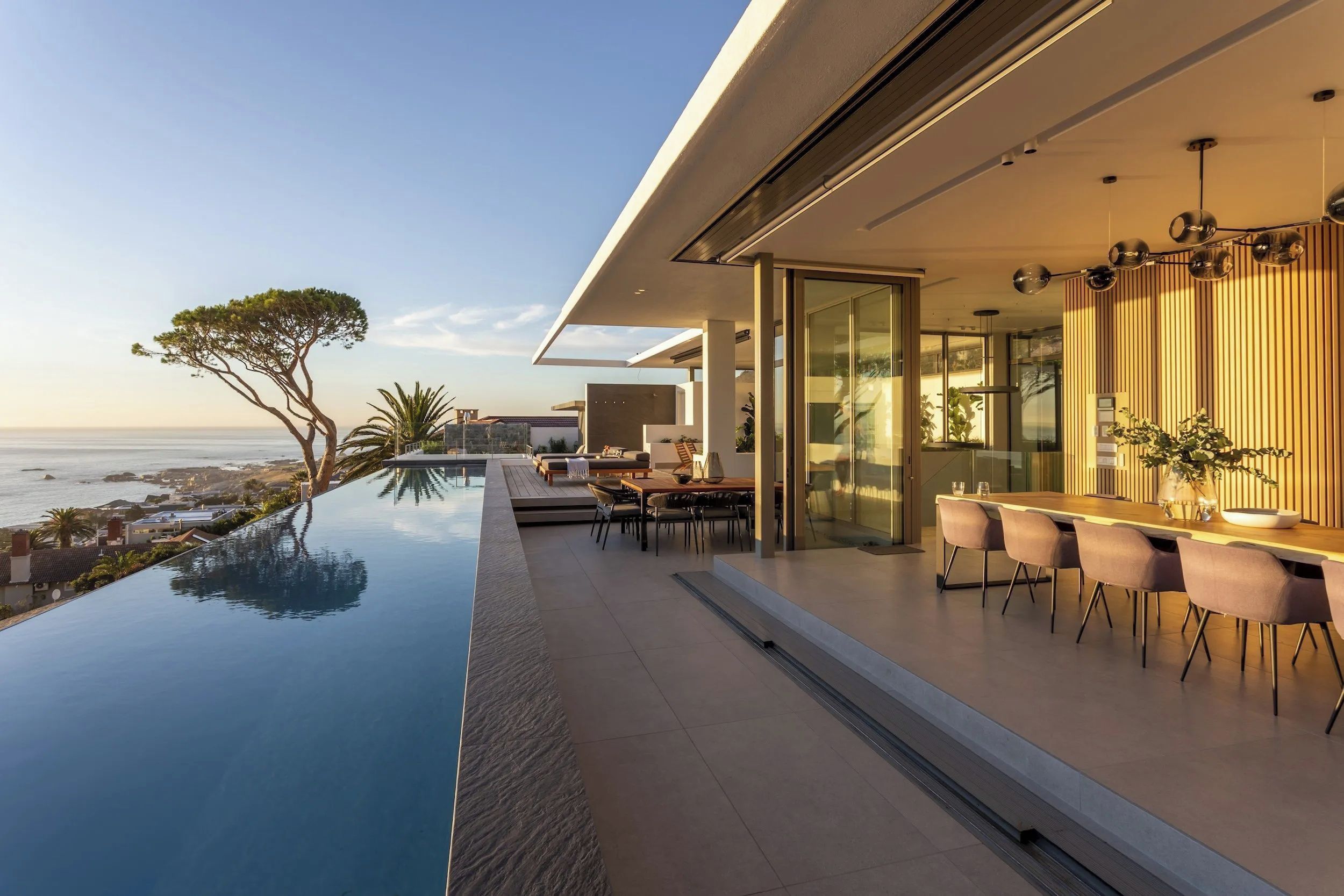 A modern outdoor dining area with a pool, overlooking a coastal landscape.