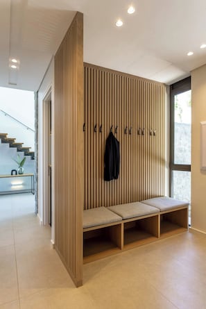 Un interior moderno con un separador de madera, un banco con cojines y un perchero.