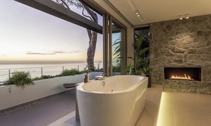 Un baño moderno con una bañera grande, una chimenea de piedra y vistas al océano.