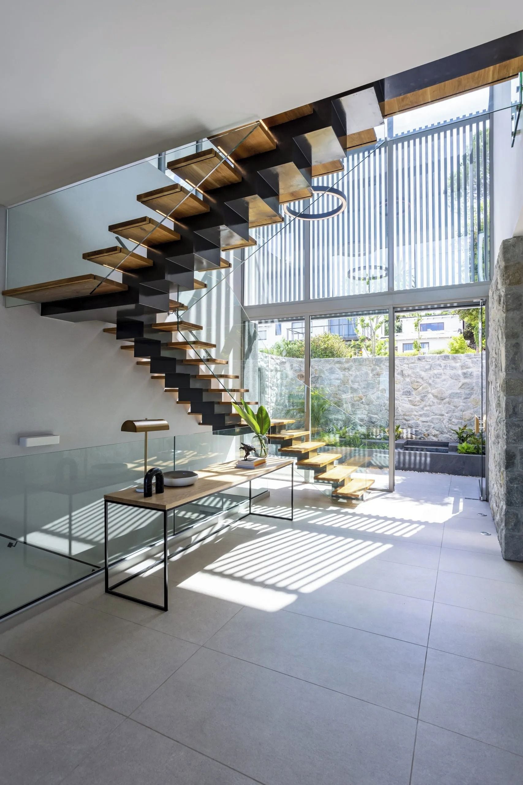A modern interior with a spiral staircase, glass railings, and a view of the outdoors.