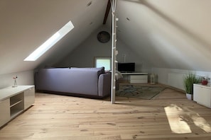 An attic room with a sloped ceiling, a sofa, a TV, a small table, and a radiator. - Holiday home in Detmold with swimming pool (Detmold)