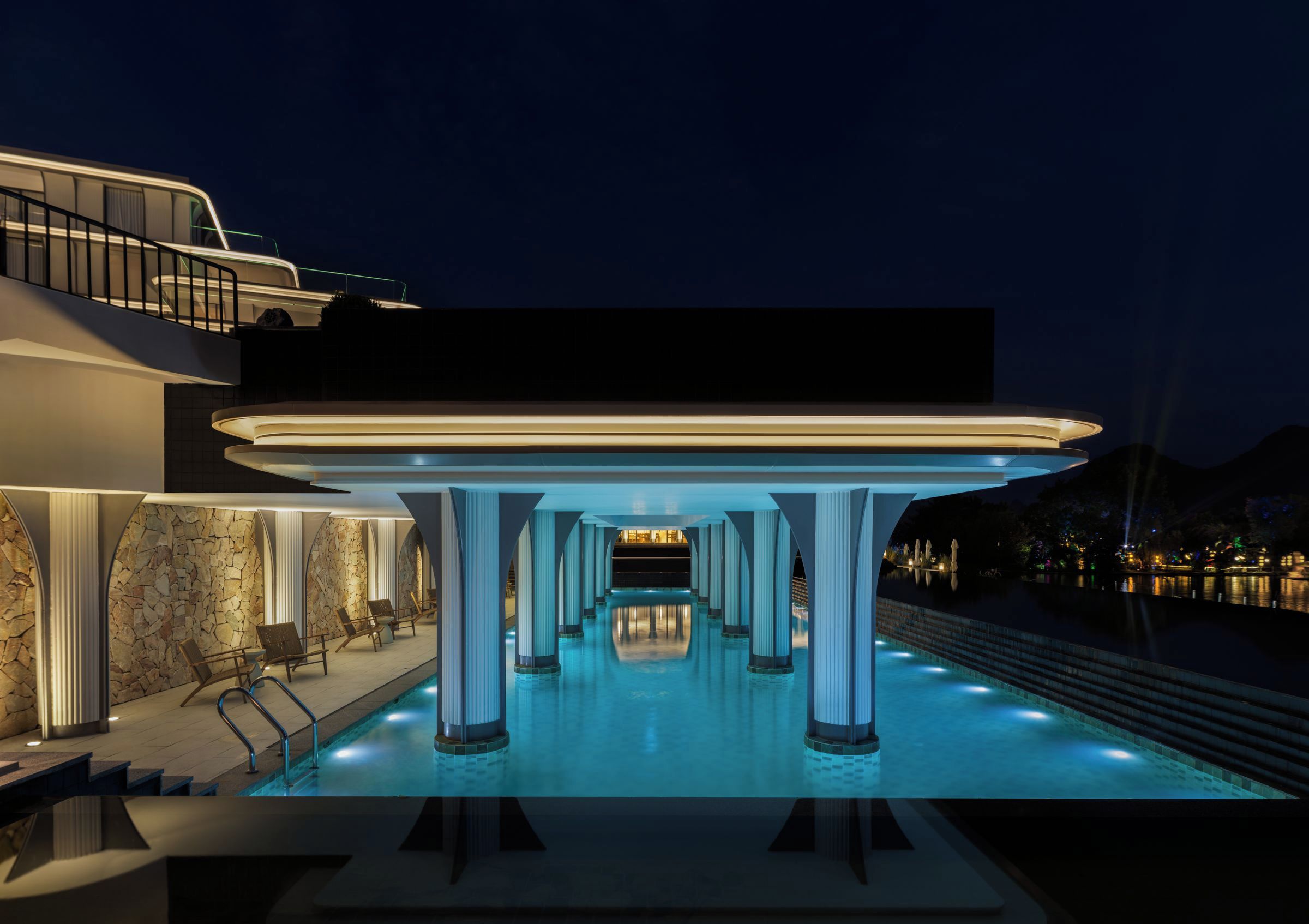 A modern building with a pool area, columns, and a staircase leading to a balcony.