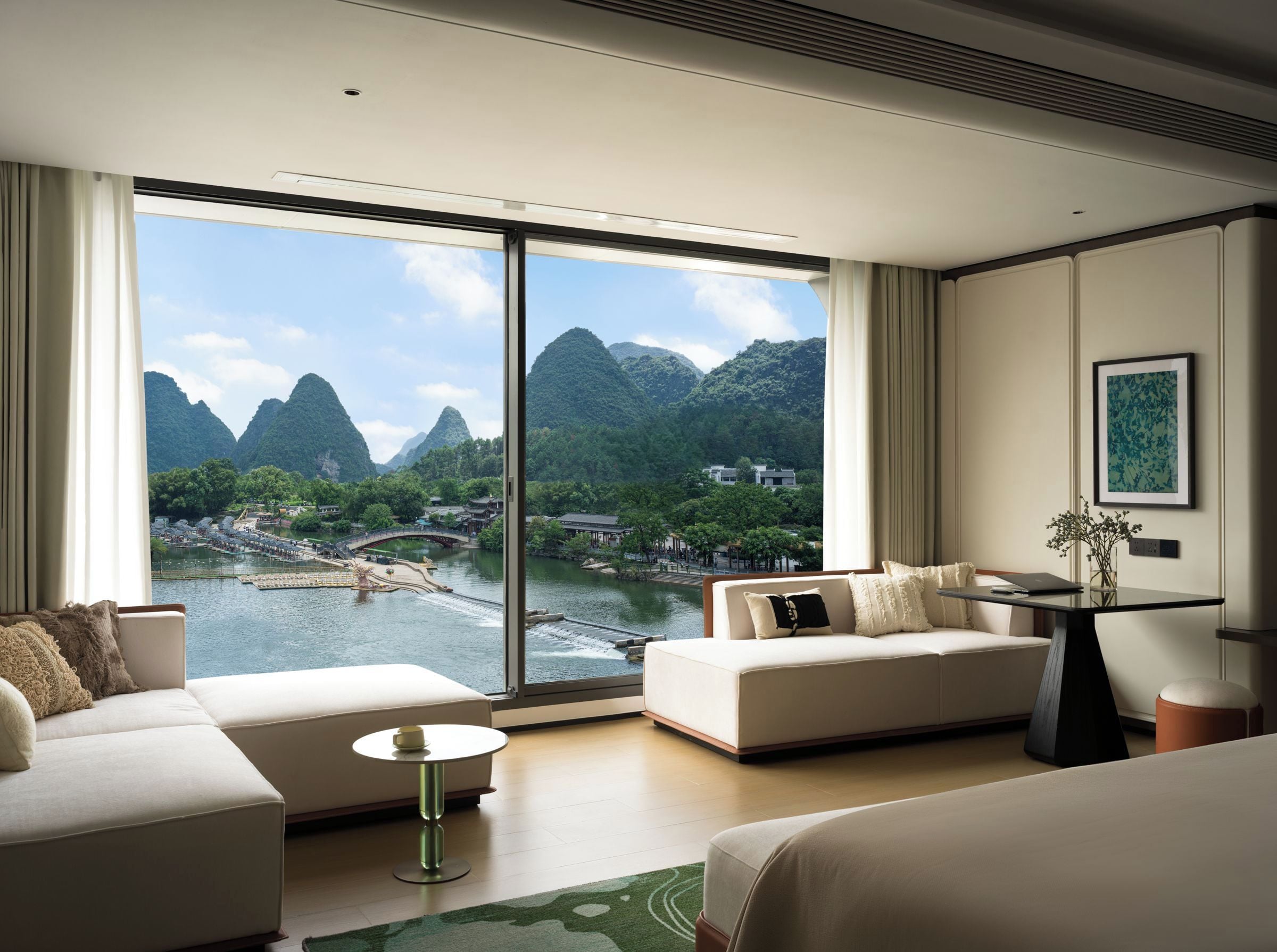 A modern hotel room with a large window offering a view of a river and mountains.