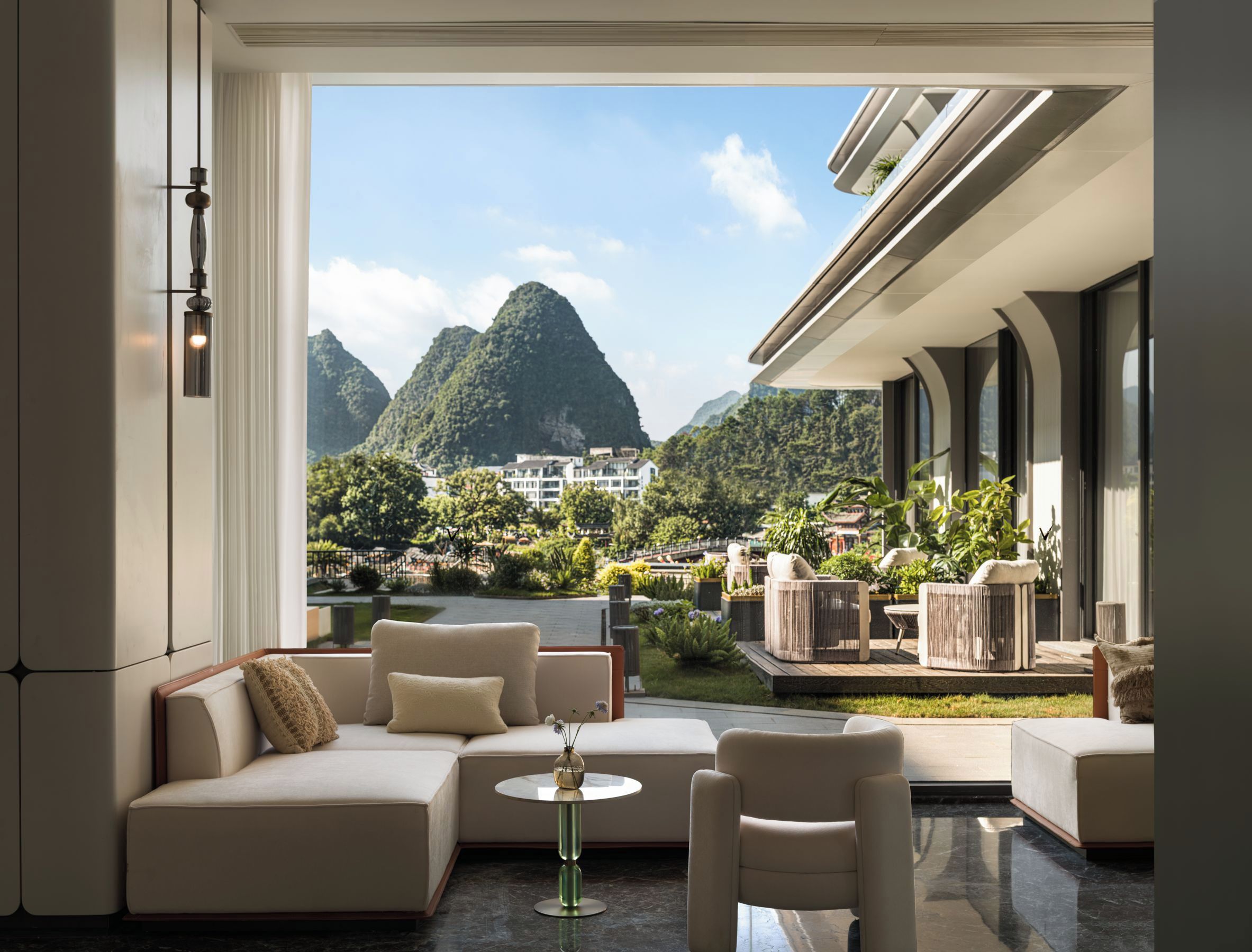 A modern interior with a sofa, chairs, and a table, overlooking a mountainous landscape.