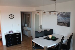 A modern dining area with a white table, black chairs, a candle, and a painting on the wall. - Holiday apartment with 1 bedroom (Westerland)