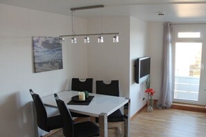 A dining area with a white table, black chairs, a flat-screen TV, and a painting on the wall. - Holiday apartment with 1 bedroom (Westerland)