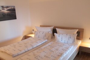 A double bed with a wooden headboard, two bedside tables, and a wall-mounted picture. - Holiday apartment with 1 bedroom (Westerland)