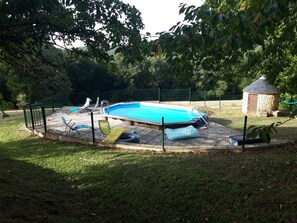 En inhägnad trädgård med en pool, en liten stenbyggnad och en gräsyta.