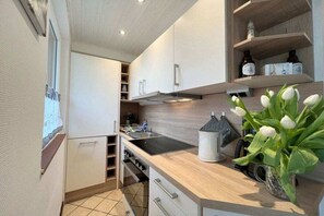 Cozinha moderna com armários brancos, forno embutido e bancada com um vaso de flores brancas.