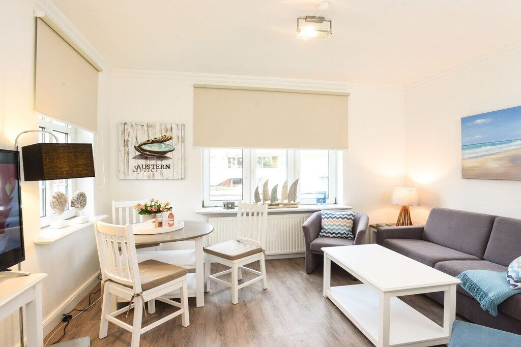 A living room with a television, a dining table with chairs, a sofa, and a window with a view.