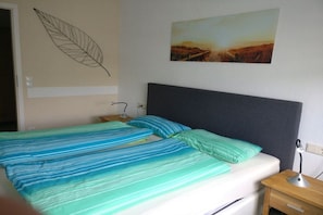 A bed with a striped bedspread, a nightstand with a lamp, a wall art piece, and a door. - 1 in the periwinkle house (Cuxhaven-Duhnen)