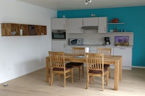 A modern kitchen with white cabinets, a microwave, and a dining area with wooden chairs and a table. - 1 in the periwinkle house (Cuxhaven-Duhnen)