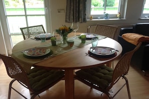 A round dining table with a green tablecloth, surrounded by four wicker chairs with green cushions. - Holiday apartment in Bad Harzburg with Wi-Fi (Bad Harzburg)