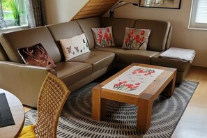A modern living room with a brown leather sofa, a wooden coffee table, and a woven chair. - Holiday apartment in Bad Harzburg with Wi-Fi (Bad Harzburg)