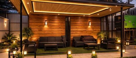 Un espacio al aire libre moderno con pared de madera, asientos acolchados e iluminación ambiental.