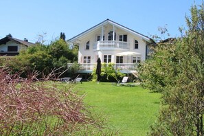 Ein großes, zweistöckiges Haus mit Balkon, umgeben von einem gepflegten Rasen und Bäumen.