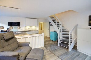A modern living room with a sofa, a staircase, and a kitchen area. - Holiday apartment with 2 bedrooms (Sankt Peter-Ording)