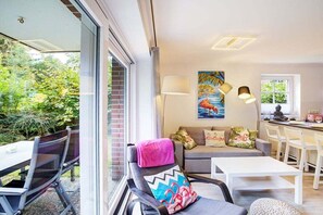 A modern living room with a sofa, chairs, a dining table, and a painting on the wall. - Holiday apartment with 1 bedroom (Sankt Peter-Ording)