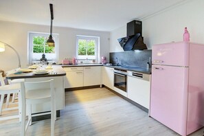 A modern kitchen with white cabinetry, a pink refrigerator, and a dining area with a table set for two. - Holiday apartment with 1 bedroom (Sankt Peter-Ording)