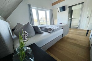 Une chambre à coucher moderne avec un lit, un vase en verre rempli de fleurs et un téléviseur fixé au mur.