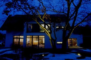 Una casa moderna con ventanas amplias y un árbol en primer plano.