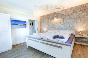 A bedroom with a bed, a television, a brick wall, and a decorative light fixture. - Villa by the sea Apartment 2 (Sankt Peter-Ording)