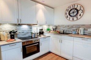 A kitchen with white cabinets, a stove, a sink, and a wall clock. - Villa by the sea Apartment 2 (Sankt Peter-Ording)
