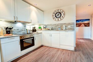 Une cuisine moderne avec des armoires blanches, un four encastré, une horloge et un crédence au style rustique.