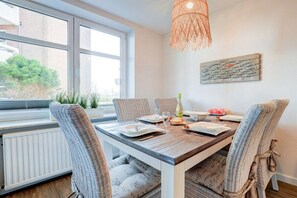 Un coin repas avec une table en bois, des chaises en osier et une vue dégagée sur l’extérieur grâce à une grande fenêtre.