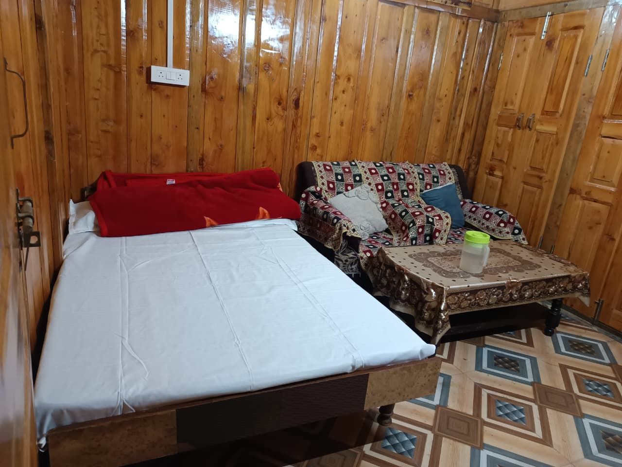 Quarto de madeira com uma cama, um sofá e uma pequena mesa com toalha de mesa estampada.