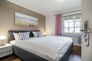 A bedroom with a bed, bedside tables, a window with curtains, a wall-mounted mirror, and a painting. - Holiday apartment in Sylt with 1 bedroom (Keitum)