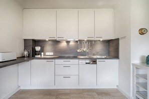 A modern kitchen with white cabinetry, a marble backsplash, and built-in appliances. - Holiday apartment in Sylt with 1 bedroom (Keitum)