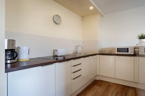 A modern kitchen with white cabinets, a wooden countertop, a coffee maker, a toaster, a microwave, and a clock on the wall. - Apartment in Westerland with swimming pool (Westerland)