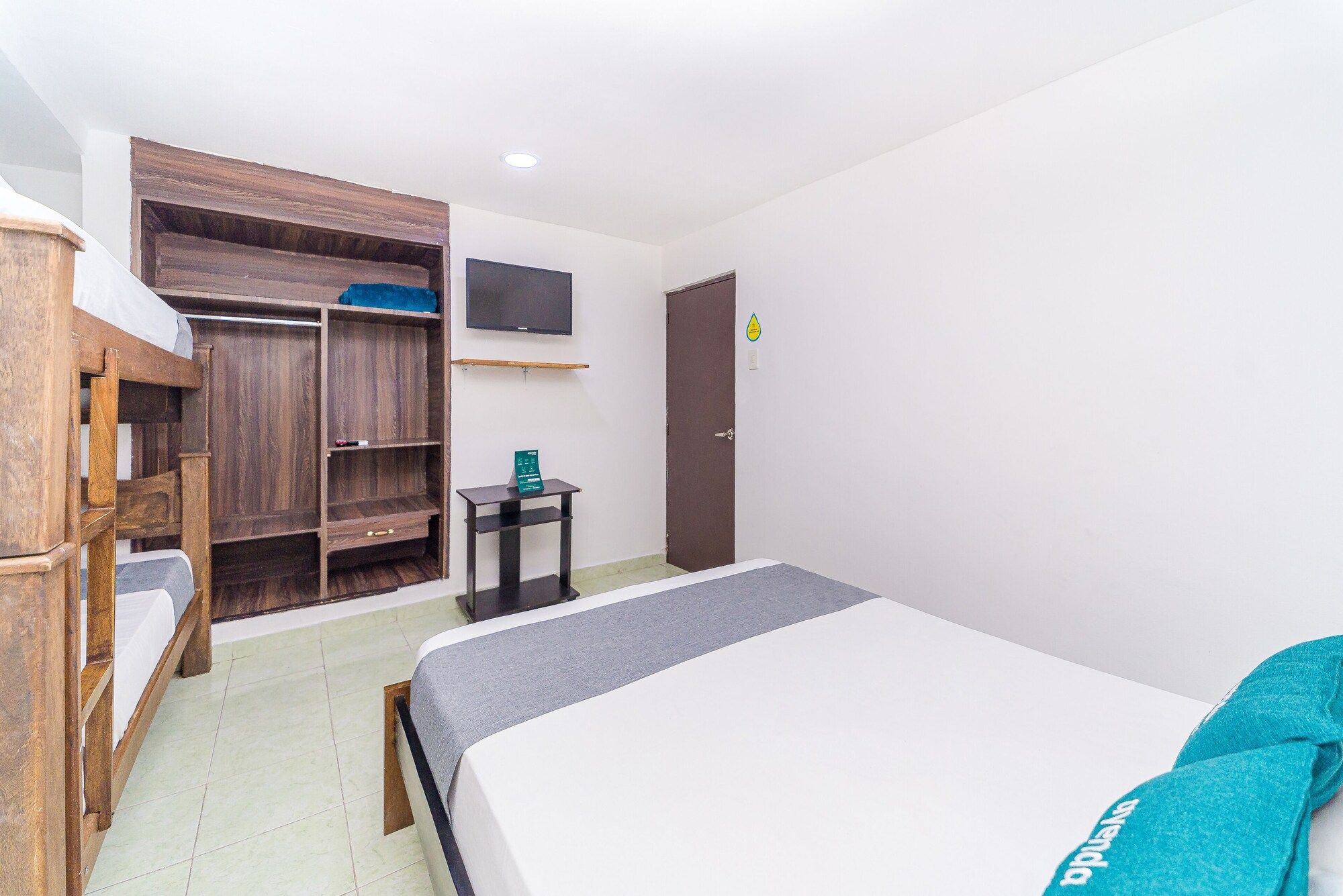 A hotel room with a bed, a wooden wardrobe, a small table, and a television on the wall.