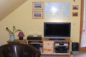 Un salón con televisión sobre un mueble de madera, un mapa en la pared y una planta en maceta.