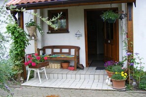 A wooden bench outside a building with a tiled porch, potted plants, and a welcome sign. - Holiday apartment with 2 bedrooms (Bentwisch)