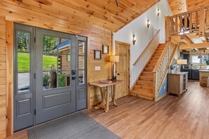 A wooden interior with a staircase, a door with a view, and a small table with a lamp. - Ski, Relax & Unwind—6BR Retreat Near Wisp (McHenry)