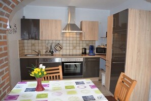 Eine kleine Küche mit Herd, Backofen, Mikrowelle und Spüle. Ein Esstisch mit bunten Tischdecken und eine Vase mit Blumen.