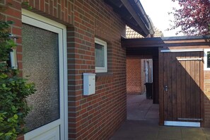 A brick building with a white door, a small window, and a wooden gate. - Holiday home North Sea Pearl (Hooksiel)