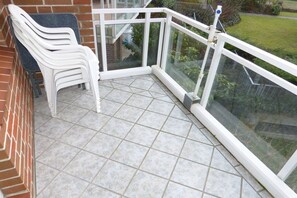 Ein Balkon mit Glasgeländer, einem weißen Plastikstuhl und einem gefliesten Boden.