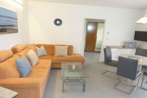 Ein Wohnzimmer mit einer Couch, einem Glastisch und einem Essbereich mit Tisch und Stühlen.