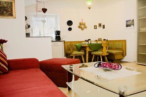 A living room with a red sofa, a glass coffee table, and a dining area with a green tablecloth. - Holiday apartment with 1 bedroom (Schönau am Königssee)