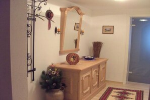 A hallway with a wooden cabinet, a mirror, a vase with flowers, and a patterned rug. - Holiday apartment with 1 bedroom (Schönau am Königssee)