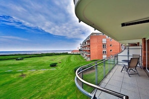 A balcony with a view of a green lawn and a brick building in the background. - Strandpalais, Apt. 209 (Cuxhaven)